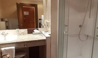 A modern bathroom with a shower and a sink. The walls are in neutral colors and the floor has dark tiles.