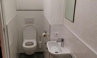 A modern bathroom with a toilet and a small sink. The walls are light and the tiles are in a simple design.