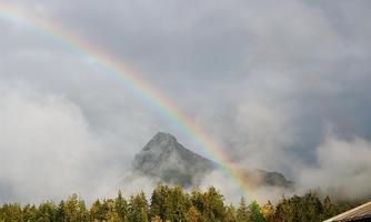 A beautiful rainbow over the mountains in a wooded landscape. In the foreground, cozy wooden cabins can be seen.