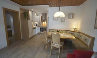 A cozy dining area with a round table and benches. The modern kitchen is open and well-lit.