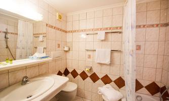 A bright bathroom with white tiles and a shower cabin. There is a sink, towels, and some toiletries.