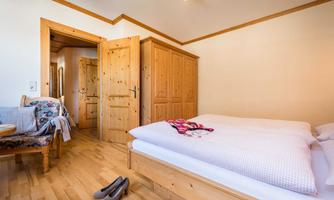 A cozy bedroom with wooden furniture and a double bed. Next to the bed there is a chair and a pair of shoes on the floor.