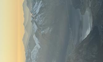 An impressive mountain landscape with snow-capped peaks and a serene lake. The sky is tinted in soft colors at sunset.