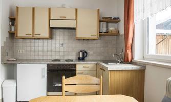 A bright kitchen with modern furniture and a wash basin. The table is in the center and there are windows with curtains.