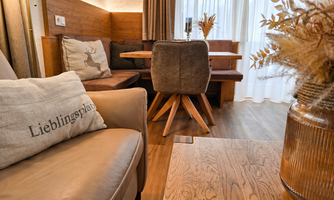 A cozy living area with a beige armchair and a wooden table. The decor is modern with soft colors and decorative plants.