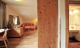 A cozy room in the attic with wooden details and a seating area. There is also a view into the bathroom.