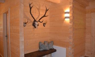 A cozy room with wood paneling and a small bench. Antler parts hang on the wall, and a modern lamp provides lighting.