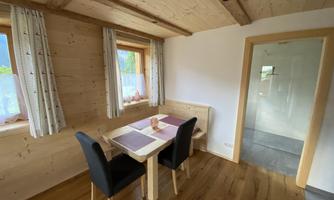 A cozy dining area with a table and four chairs. The warm wooden walls and windows create a friendly atmosphere.