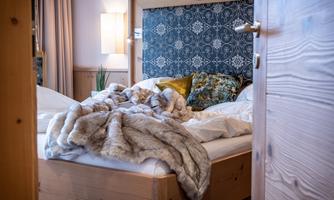 A cozy bedroom with a wooden bed and a decorative headboard. On the bed lies a soft, gray blanket and pillows in various colors.
