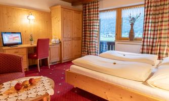 A cozy bedroom with two beds and a desk. The room has wooden furniture and large windows overlooking the landscape.