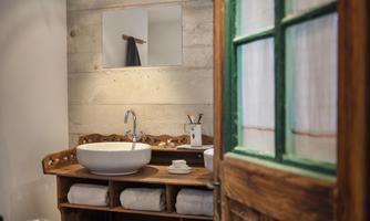 A modern bathroom with an elegant sink and wooden shelves. The glass panel above the sink reflects a stylish and clean atmosphere.