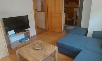 A cozy living area with a blue sofa and a wooden table. In the background, an open door can be seen leading into another room.