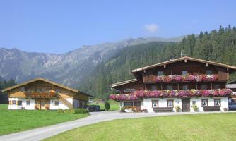 A beautiful Alpine farmhouse with a balcony and colorful flowers. In the background, majestic mountains rise under a clear blue sky.