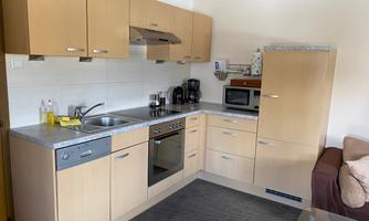 A modern kitchen with light wooden cabinets and modern appliances. The sink, stove, and microwave are well arranged on the countertop.