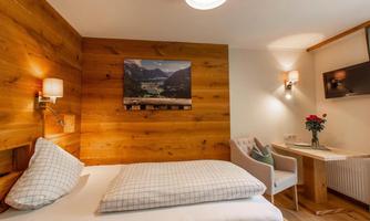A cozy hotel room with wooden walls and a single bed. A desk with a chair and a decorative flower arrangement completes the space.