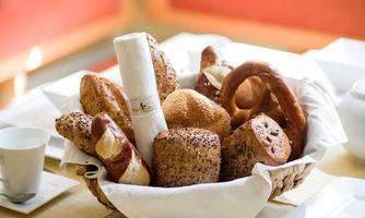 A basket with various rolls and pastries. Among them are pretzels and a filled roll.