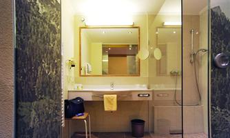 A modern bathroom with a clear sink and a large mirror. The shower is separated by a glass wall, and there is a cozy seating area.