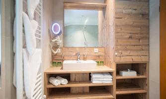 A modern bathroom with wooden paneling and elegant sanitary ware. Fresh towels are laid out on the sink, and a large mirror creates a bright atmosphere.