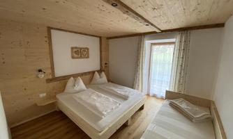 A cozy room with two beds and wooden-paneled walls. Large windows provide plenty of daylight.