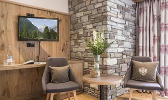 A cozy seating area with two chairs and a table. The wall is clad with stones, and a television is mounted on it.