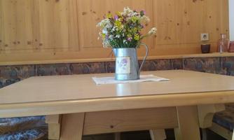 A wooden table with a bouquet of flowers in a vase. Around the table, there are chairs with gray patterned seats.