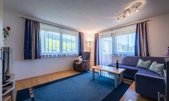 A modern living room with a blue carpet and a comfortable couch. Large windows provide plenty of natural light and a cozy atmosphere.
