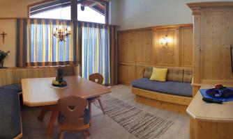 A cozy room with wooden paneling, a dining table, and a seating area. Large windows let in plenty of light, and the windows are decorated with colorful curtains.