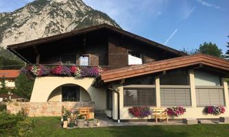 A charming house with blooming balcony boxes in front of an impressive mountain panorama. The sunny garden offers an inviting atmosphere.