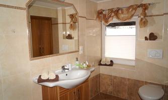A cozy bathroom with a modern sink arrangement and a large mirror. The walls are bright, and there are decorative towels as well as a windowsill with small accessories.