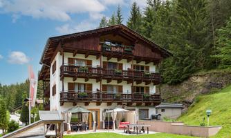 A charming hotel in alpine style with several balconies. Surrounded by green forests and a sunny atmosphere.