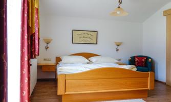 A cozy bedroom with a large double bed and wooden decor. The room has bright walls and exudes a relaxed atmosphere.