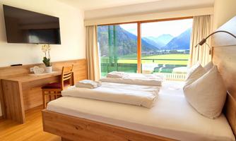 A modern hotel room with two beds and a television. Large windows offer a view of the mountains and the green landscape.