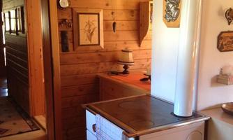 A cozy kitchen with wood paneling and a white stove. Some decorative elements and clocks are visible on the wall.