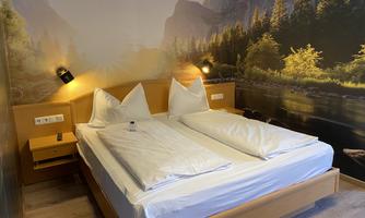 A modern bedroom with a large double bed and white bedcovers. A picturesque natural landscape is depicted on the wall.