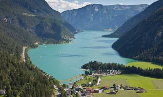 A picturesque landscape with a clear, blue lake, surrounded by tall mountains and lush forests. In the foreground, there is a small village with houses and meadows.
