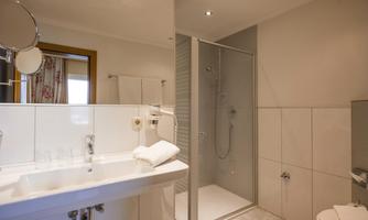 A modern bathroom with a shower and sink. The walls are light tiled, and there are towels on the sink.