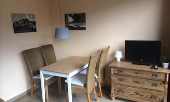 A simple dining room with a wooden table and four chairs. Two pictures hang on the wall, and a television stands on a dresser.