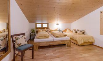 A cozy bedroom with two beds and wood paneling. The room is bright and inviting, with a nice fireplace chair and warm colors.