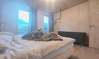 A cozy bedroom with a bed and soft pillows. Large windows offer a view outside and let in plenty of light.