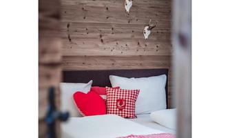 A cozy bedroom with wooden paneling and rustic decorative elements. The cushions in red and white give the room an inviting atmosphere.