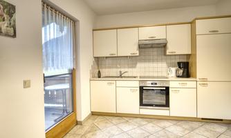 A modern kitchen with white cabinets and an elegant countertop. Natural light comes through the window and there is access to a balcony.