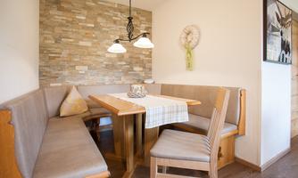 A cozy dining area with a wooden bench and a table. The walls are decorated with stone cladding, and there is soft lighting.