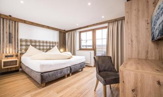 A modern bedroom with a large bed and wooden details. There is a chair and a television on the wall.