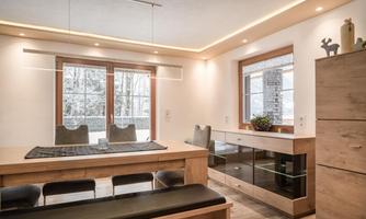 A modern interior with a large dining table and elegant chairs. Large windows allow plenty of daylight in and provide a view of the outdoor landscape.
