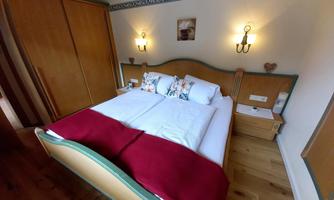 A cozy bedroom with a double bed, decorated with white pillows and a red blanket. Elegant lamps and wooden cabinets are located on the walls.