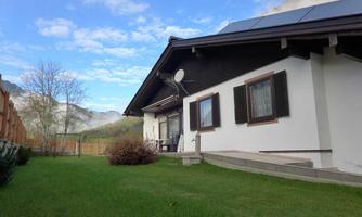 A modern house with a beautiful garden and a terrace. In contrast, the sky is clear and the mountains are visible in the background.