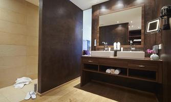 A modern bathroom with a large mirror and two sinks. The floor is made of wood and there is a towel on the floor.