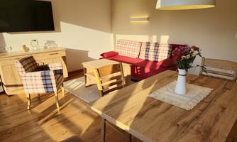 A cozy living room with a red couch and a wooden table. The light falls gently through the window and illuminates the furnishings.