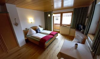 A cozy room with two beds and wooden floors. Large windows provide plenty of natural light.