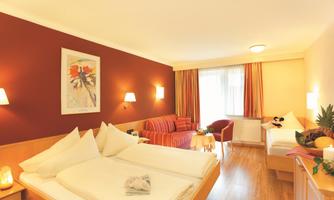 A comfortable hotel room with two beds and a cozy seating area. The walls are designed in warm colors, and the room is well lit.